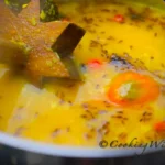 Trinidad dhal simmering in a pot with roasted cumin seeds, hot peppers and a wooden swizzle stick(dhal ghutney).